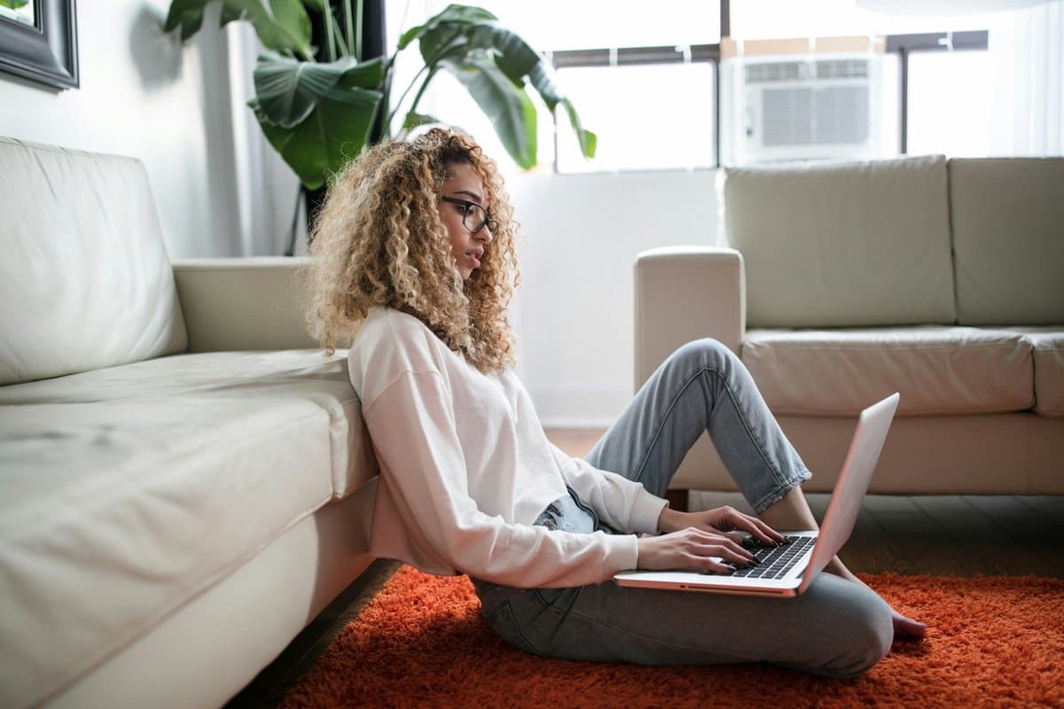 Woman leaning against a sofa, watching the stream on her laptop